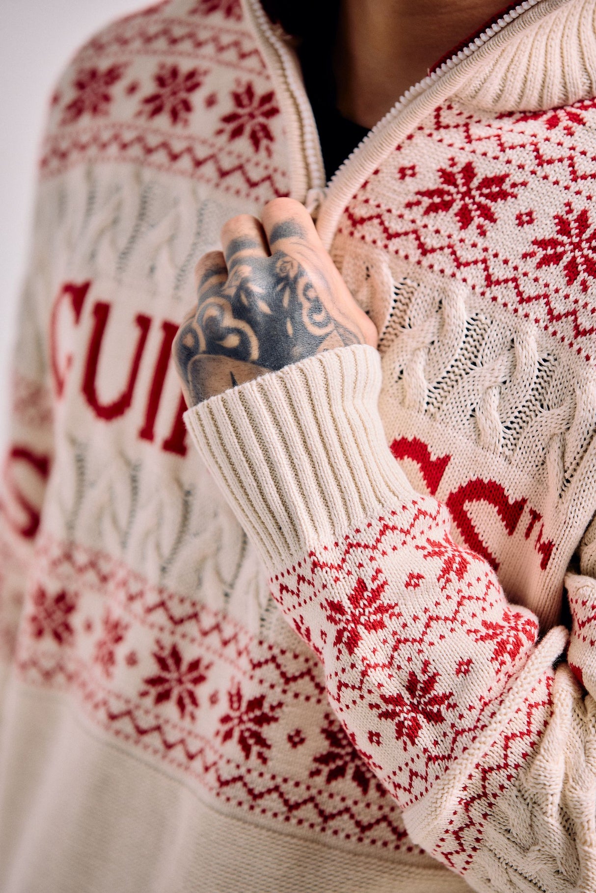 Close-up of a person wearing a cream-colored sweater with red snowflake patterns and text.