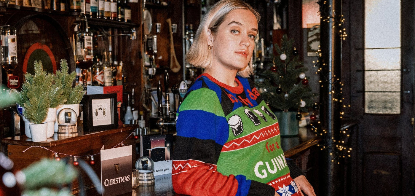 Person wearing a festive sweater with Christmas-themed designs in a bar setting