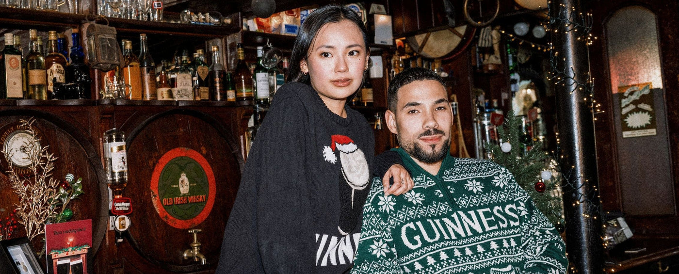 Two people wearing Christmas-themed sweaters in a bar setting.
