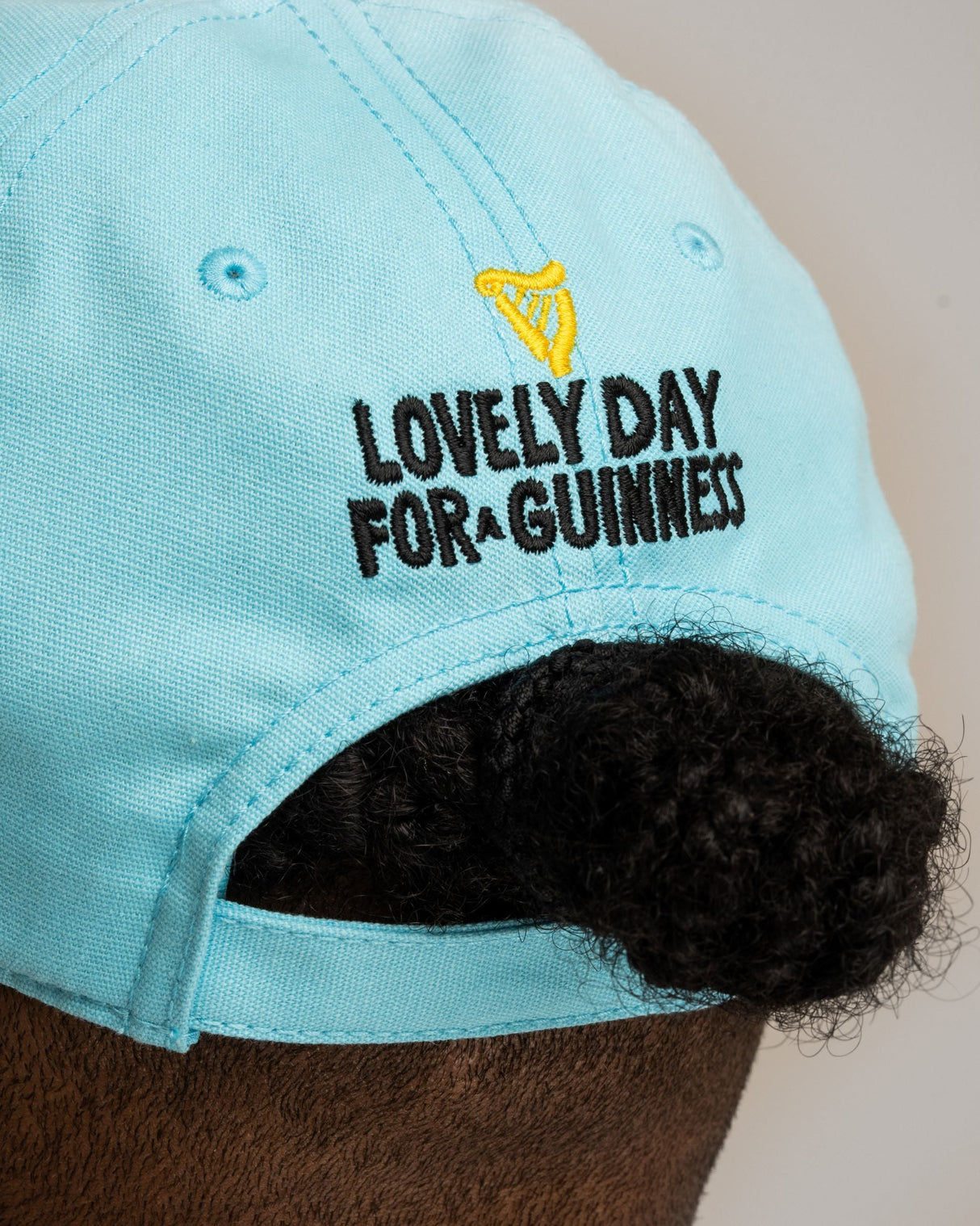 Light blue cap with 'Lovely Day for Guinness' text worn by a person.