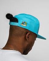 Person wearing a turquoise cap with a logo on a plain background