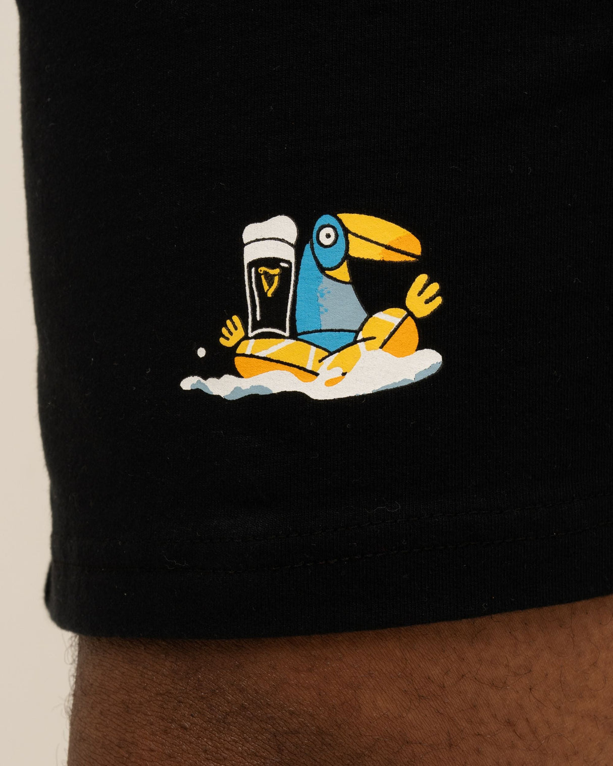 Black shorts with a colorful toucan holding a beer graphic on a beige background