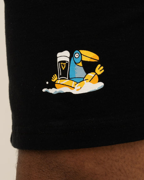Black shorts with a colorful toucan holding a beer graphic on a beige background