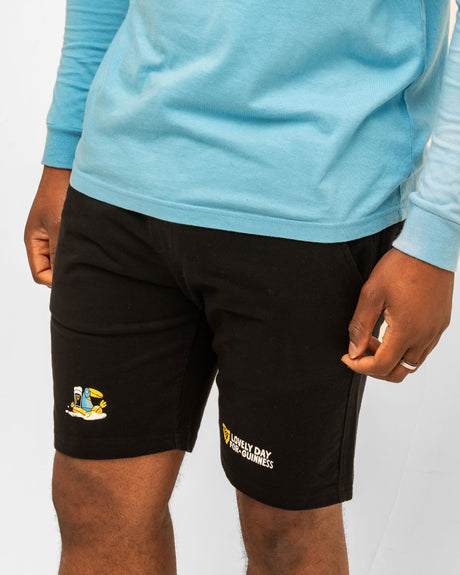 Person wearing black shorts with logos on a light gray background