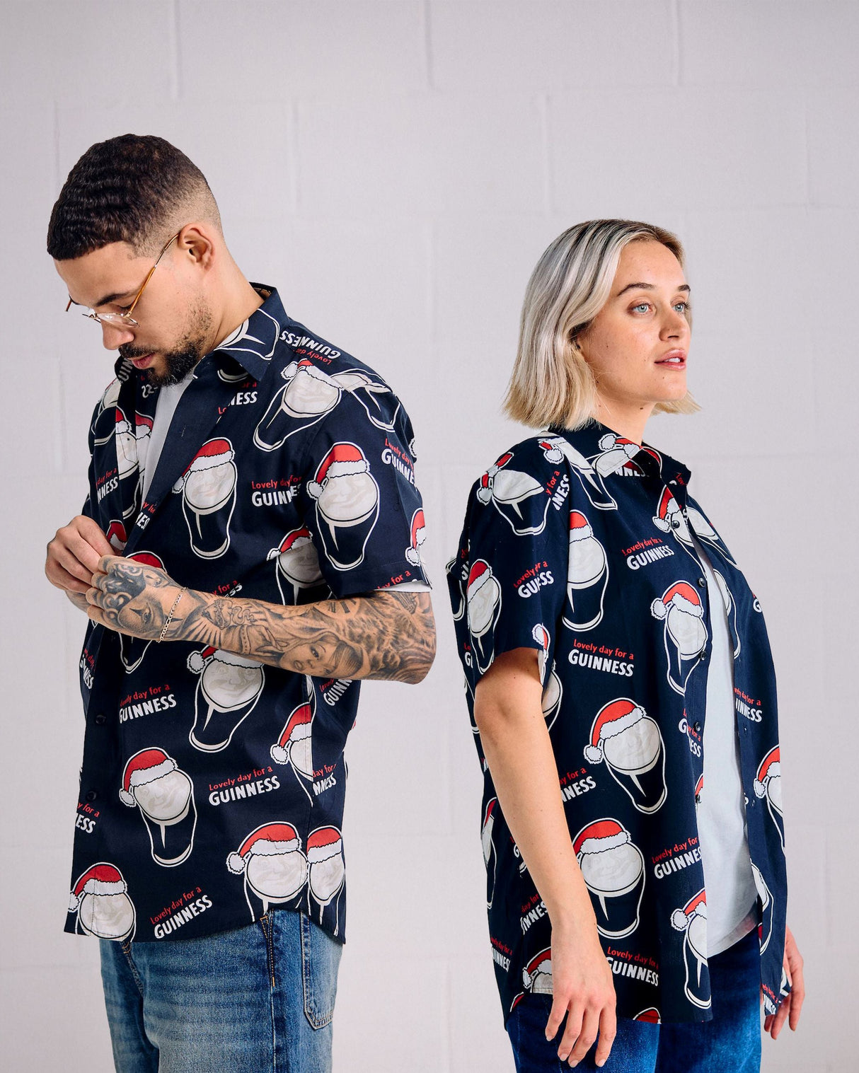 Two people wearing navy blue shirts with red and white Guinness beer bottle and hat pattern against a white background.