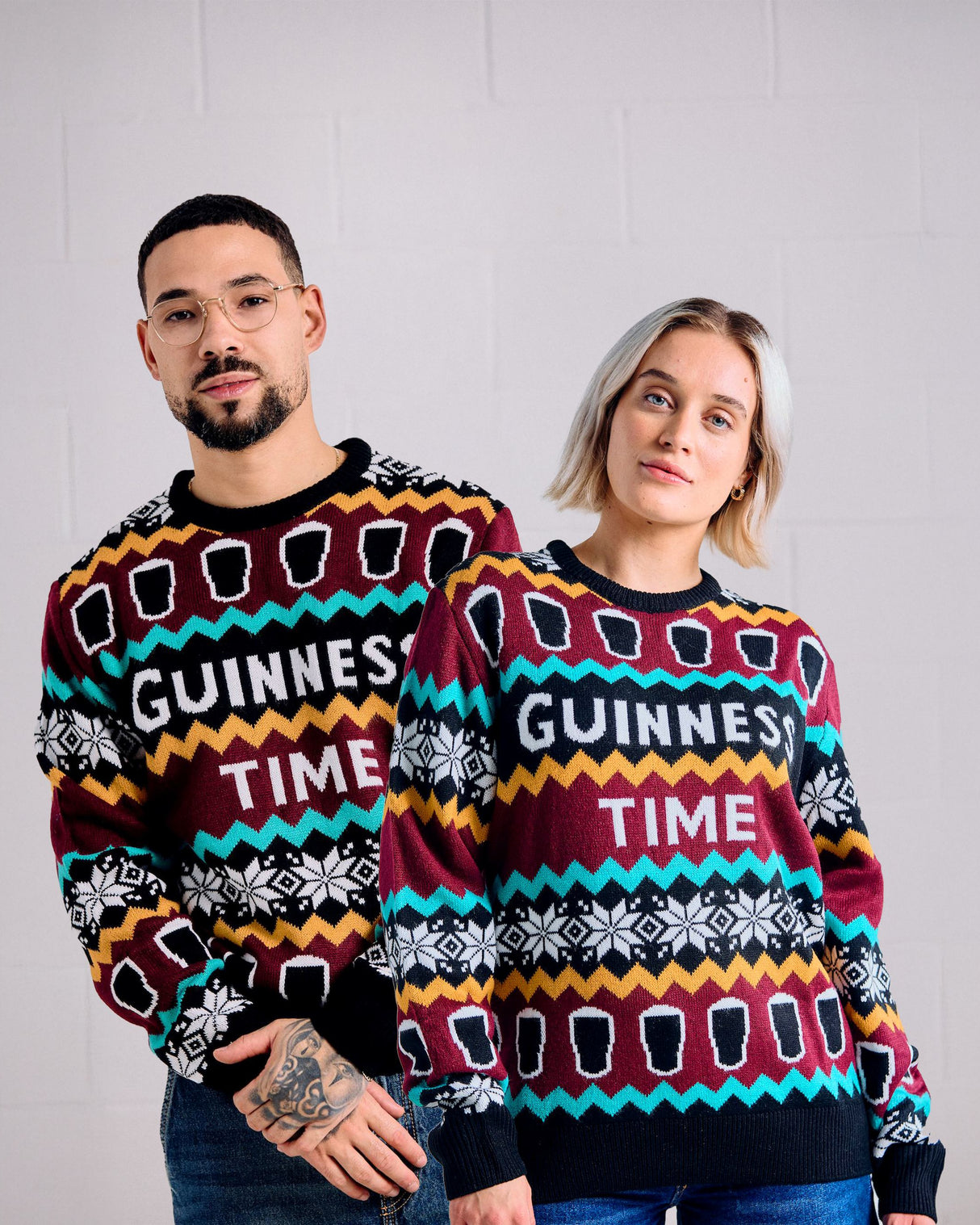 Two people wearing colorful Guinness-themed sweaters against a plain background