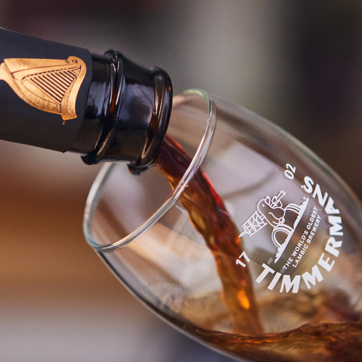 Image of bottle pouring Guinness x Timmermans Lambic and Stout into a flute glass.