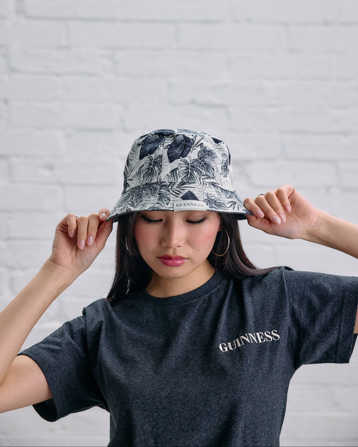 Person wearing a floral bucket hat and a Guinness t-shirt against a white brick wall.