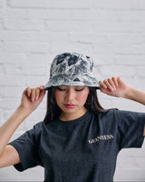 Person wearing a floral bucket hat and a Guinness t-shirt against a white brick wall.