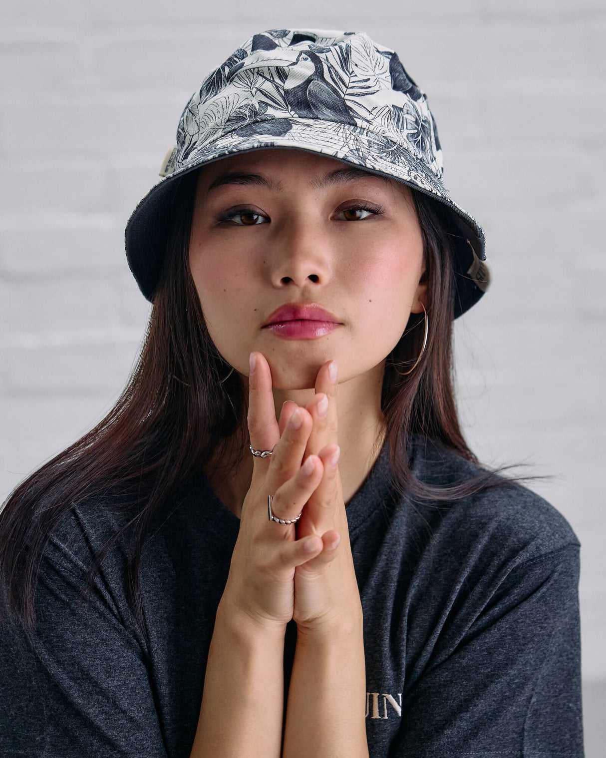 Woman wearing a patterned bucket hat and dark t-shirt against a gray background