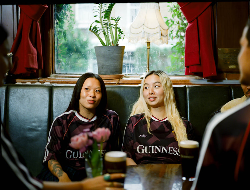 Two women in Guinness jerseys sitting at a table with drinks in a cozy indoor setting.