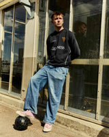 Person wearing a black Guiness sweatshirt and blue jeans sitting on a ledge.