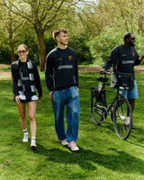 Three people walking outdoors with a bicycle, wearing Guinness-branded clothing.