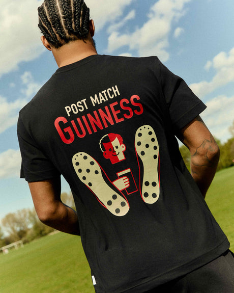 Person wearing a black t-shirt with 'Post Match Guinness' text and graphics on the back, standing outdoors.