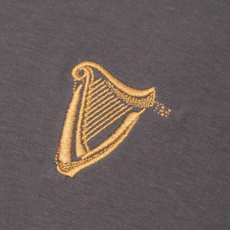 Detail of the Guinness Storehouse Exclusive dark grey t-shirt's golden harp. 